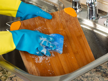 Cleaning Wooden Cutting board inside of Kitchen Sink with sponge