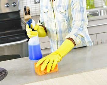 Cleaning shortcuts for every room. Woman with spray bottle and sponge cleaning kitchen counter.