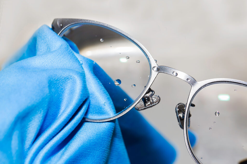 A pair of silver eyeglasses getting cleaning with a cleaning solution and a blue cloth.